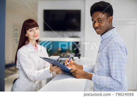 African American man patient signing an insurance contract at reception desk at the modern clinic. 79024098