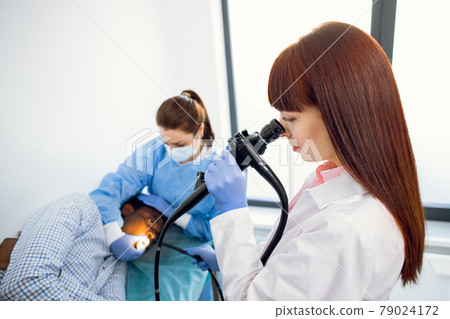 Female European doctor, looking in endoscope camera, doing stomach examination of male patient 79024172