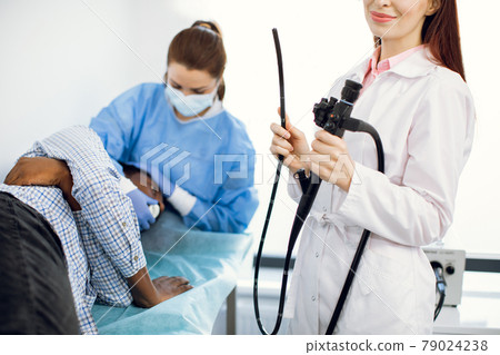 Female young doctor holding endoscope. Afro-American male patient lying on the couch and nurse 79024238