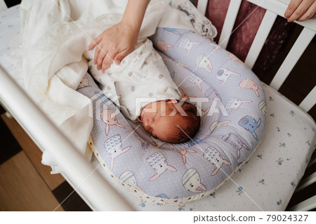 Mom's hands straighten the blanket at the sleeping in the crib of the newborn.  79024327