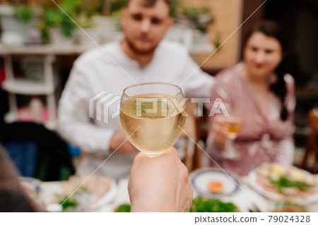 hand with a wine in focus against the backdrop of a blurred man and woman 79024328