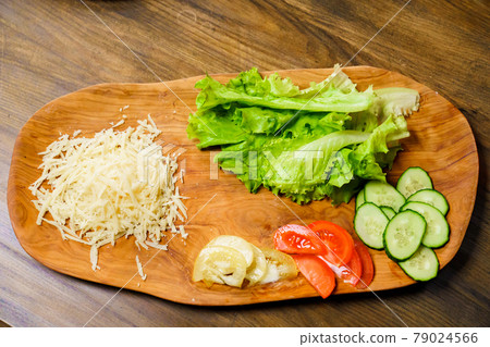 grated cheese, lettuce, ringed tomato and cucumber on a wooden cutting board. 79024566