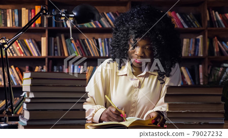 African-American woman writes in notebook in public library African-American woman writes in notebook in public library 79027232