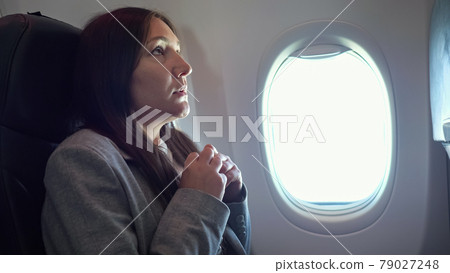 Young woman is very afraid of flying on an airplane Young woman is very afraid of flying on an airplane 79027248