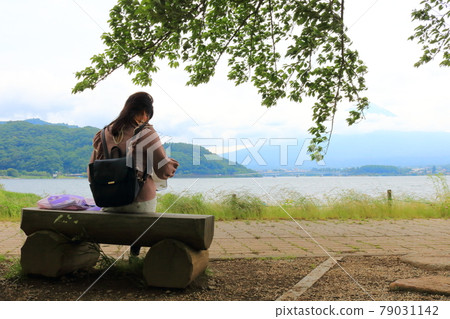 Back view of a woman sitting on a bench on the shore of Lake Kawaguchiko 79031142