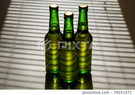 Three green glass beer bottles in the shade of the blinds. 79031871