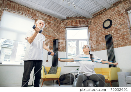 Aged man training with dumbbell while woman with rubber band 79032691