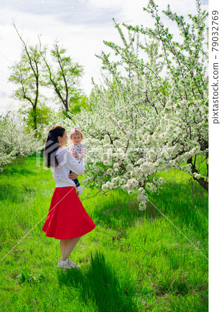 mom spinning with a daughter in her arms in the park by a flowering tree. mom spinning with a daughter in her arms in the park by a flowering tree. 79032769