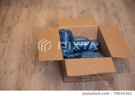 Glassware wrapped with blue wrapping nylon at the bottom of a cardboard box. Glassware wrapped in a box 79034362
