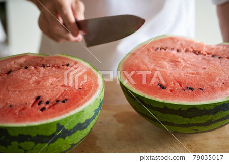 A man cutting a watermelon in the kitchen 79035017
