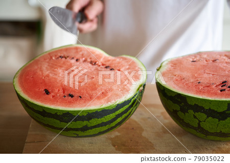 A man cutting a watermelon in the kitchen 79035022