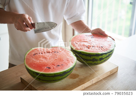 A man cutting a watermelon in the kitchen 79035023