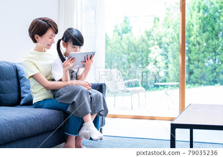 Mother hugging and watching over a girl learning online 79035236
