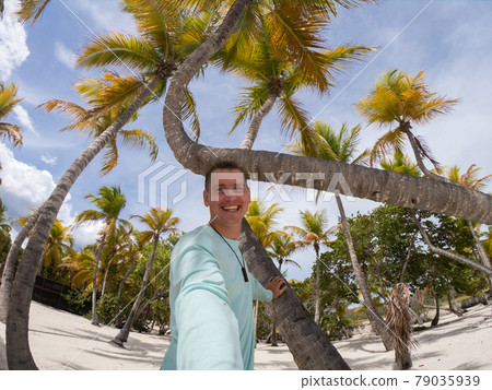 Happy smiling man taking selfies on the beach with palm trees. Vacation and travel concept  79035939