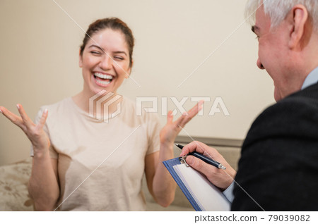 Mature gray-haired male psychotherapist with clipboard in session with female patient. Smiling caucasian woman at a psychologist appointment. Mature gray-haired male psychotherapist with clipboard in session with female patient. Smiling caucasian woman at a psychologist appointment. 79039082