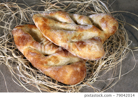 two white bread lying in straw on grey linen tablecloth 79042014