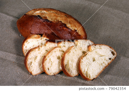 sliced white bread lying in straw on grey linen tablecloth sliced white bread lying in straw on grey linen tablecloth 79042354