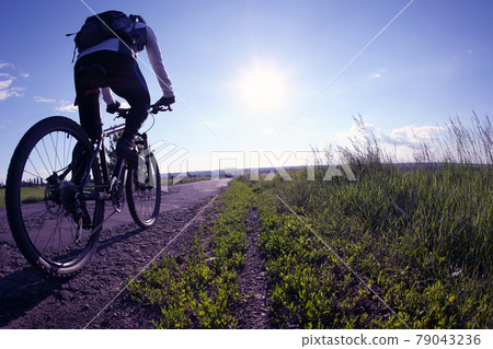 cyclist rides on the road toward the sun. cyclist rides on the road toward the sun. 79043236