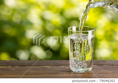 water from jug pouring into glass on table outdoors 79046262