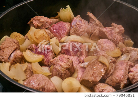 Frying the raw beef and the onions in a cauldron to prepare the Hungarian cauldron goulash. 79046851