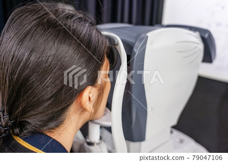 health care, medicine, people, eyesight and technology concept - Young woman checks his vision on the machine checking patient vision at eye clinic or optics store. face close-up 79047106