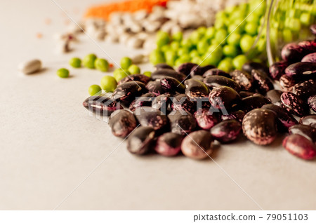 A set of different dried legumes is in glass cups and is a little scattered: red lentils, green peas, red beans, white beans. Selective Focus on Red Beans A set of different dried legumes is in glass cups and is a little scattered: red lentils, green peas, red beans, white beans. Selective Focus on Red Beans 79051103