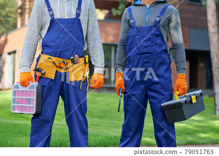 Cropped shot of two male builders in blue overalls carrying toolbox at construction site Cropped shot of two male builders in blue overalls carrying toolbox at construction site 79051763