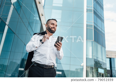 Handsome mature businessman using cellphone, walking outdoor against glass office center, empty space 79051939