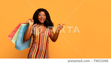Big sales. Portrait of young happy black woman with shopping bags pointing at blank space over orange background 79052006