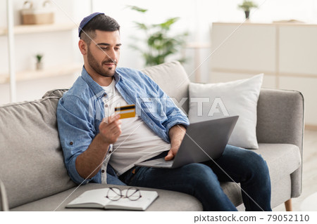 Jewish guy using pc and credit card at home Jewish guy using pc and credit card at home 79052110
