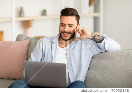 Always in touch. Young freelancer man talking on smartphone and using laptop while working remotely from home Always in touch. Young freelancer man talking on smartphone and using laptop while working remotely from home 79052128