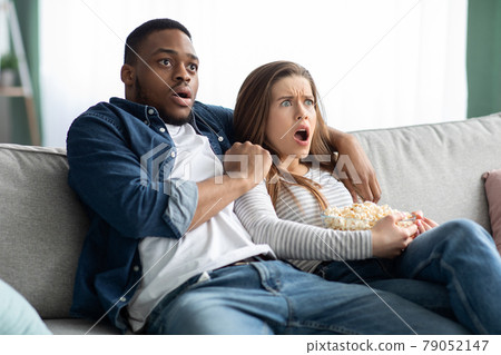 Horror Movie. Multicultural Couple Watching Scary Film And Eating Popcorn At Home Horror Movie. Multicultural Couple Watching Scary Film And Eating Popcorn At Home 79052147