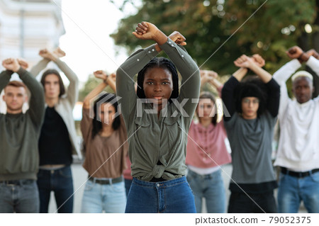 Black lady guiding multiracial group of activists, rasising fists up Black lady guiding multiracial group of activists, rasising fists up 79052375