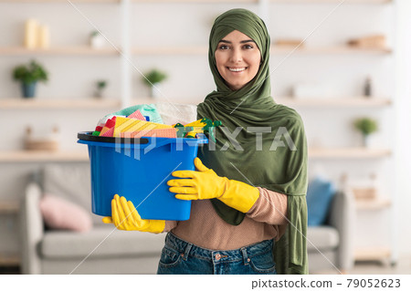 Cheerful young islamic housewife holding bucket with cleaning supplies tools Cheerful young islamic housewife holding bucket with cleaning supplies tools 79052623