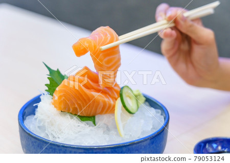 Hand holding salmon sashimi using chopsticks - Raw fresh salmon sliced served on ice with wasabi, Japanese food style. Hand holding salmon sashimi using chopsticks - Raw fresh salmon sliced served on ice with wasabi, Japanese food style. 79053124