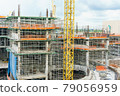 Construction site. Construction cranes and high-rise building under construction against blue sky. 79056959
