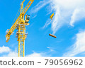 Construction site. Construction cranes and high-rise building under construction against blue sky. 79056962