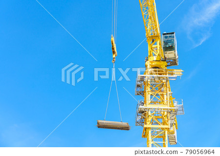Construction site. Construction cranes and high-rise building under construction against blue sky. 79056964