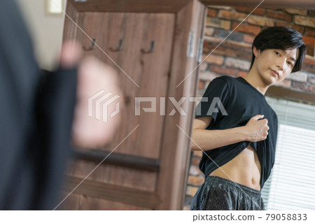 A young man checking the flesh of his stomach in the mirror 79058833