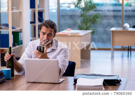 Young male alcohol addicted employee working in the office Young male alcohol addicted employee working in the office 79060160
