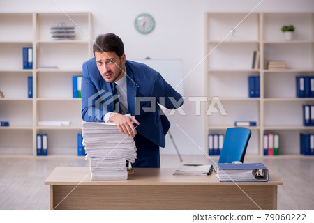 Young male employee unhappy with excessive work in the office Young male employee unhappy with excessive work in the office 79060222