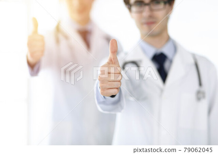 Two male doctors standing as a team and showing thumbs up as a symbol of the best service for patients in sunny clinic. Medicine concept Two male doctors standing as a team and showing thumbs up as a symbol of the best service for patients in sunny clinic. Medicine concept 79062045