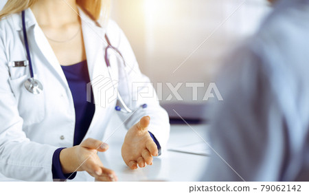 Unknown woman-doctor is talking to her patient, while they are sitting together in the sunny cabinet in a clinic. Female physician with a stethoscope at work, close-up. Perfect medical service in a Unknown woman-doctor is talking to her patient, while they are sitting together in the sunny cabinet in a clinic. Female physician with a stethoscope at work, close-up. Perfect medical service in a 79062142