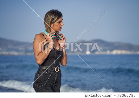 young woman dressed in black catching headphones on the beach 79063783