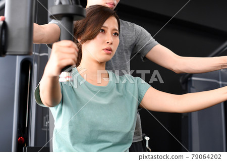 Asian women doing muscle training (chest press) on the machine and male trainers assisting Asian women doing muscle training (chest press) on the machine and male trainers assisting 79064202