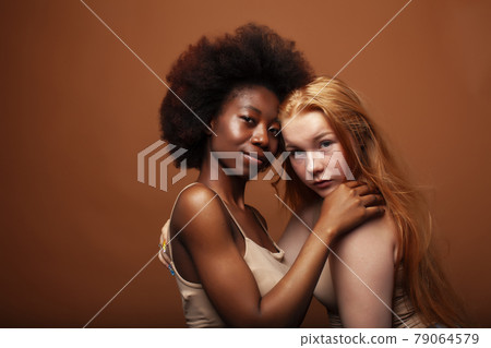 young pretty caucasian, afro woman posing cheerful together on brown background, lifestyle diverse nationality people concept 79064579