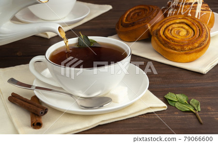 pour hot black tea into a white cup. aromatic tea with sugar and mint. delicious cinnamon rolls for breakfast. 79066600