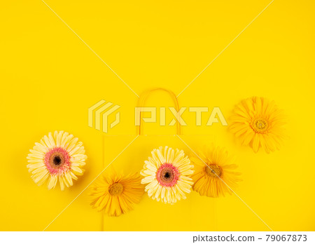 Yellow flat paper shopping bag with gerbera daisy flowers on monochrome background 79067873