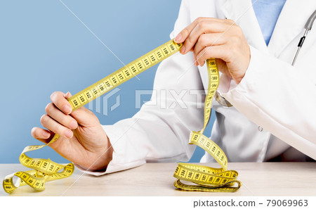 Doctor holding a yellow tape measure. Mid-section 79069963