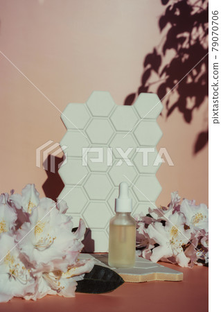 Trendy background with a bottle of natural essential oil, fresh exotic flowers, and geometric cell shapes tile with hard direct sun light and shadows on beige background. Skin care serum cosmetics. Trendy background with a bottle of natural essential oil, fresh exotic flowers, and geometric cell shapes tile with hard direct sun light and shadows on beige background. Skin care serum cosmetics. 79070706